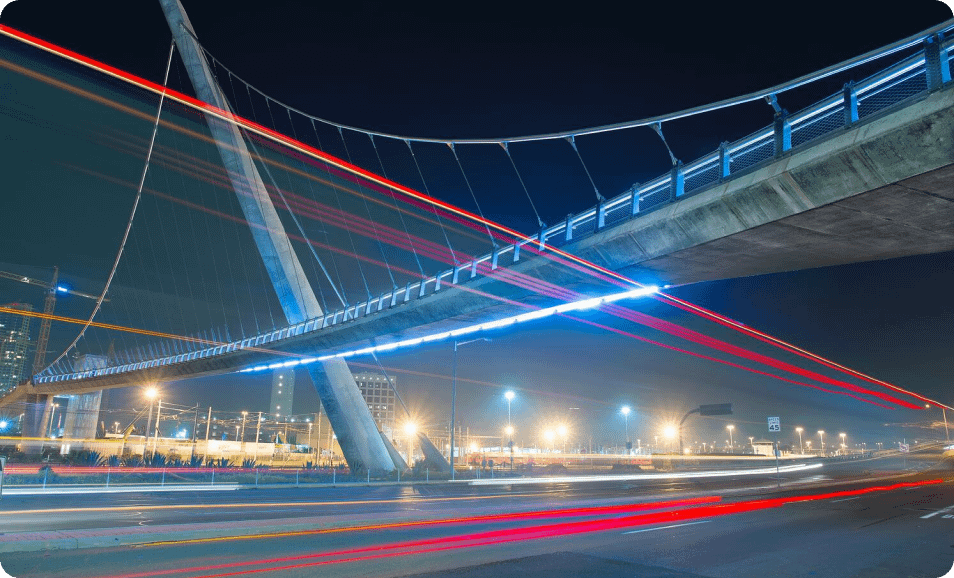 image (1) A flurry of vehicles pass beneath a bridge at lightning speed, representing how a hyperscale data center directs and manages high-volume data traffic.